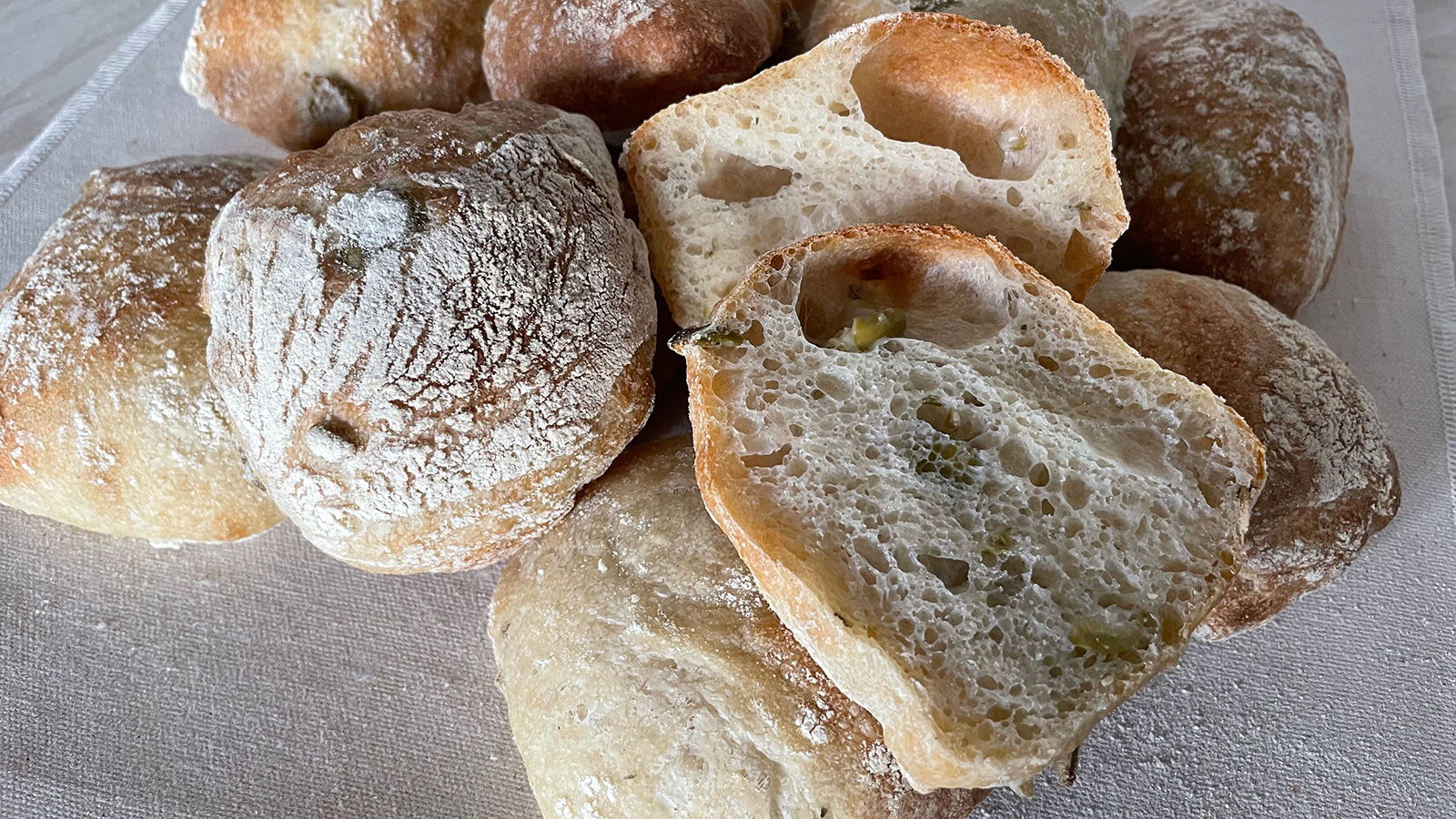 Rustic Olive Rolls arranged together with one sliced in half showing the crumb